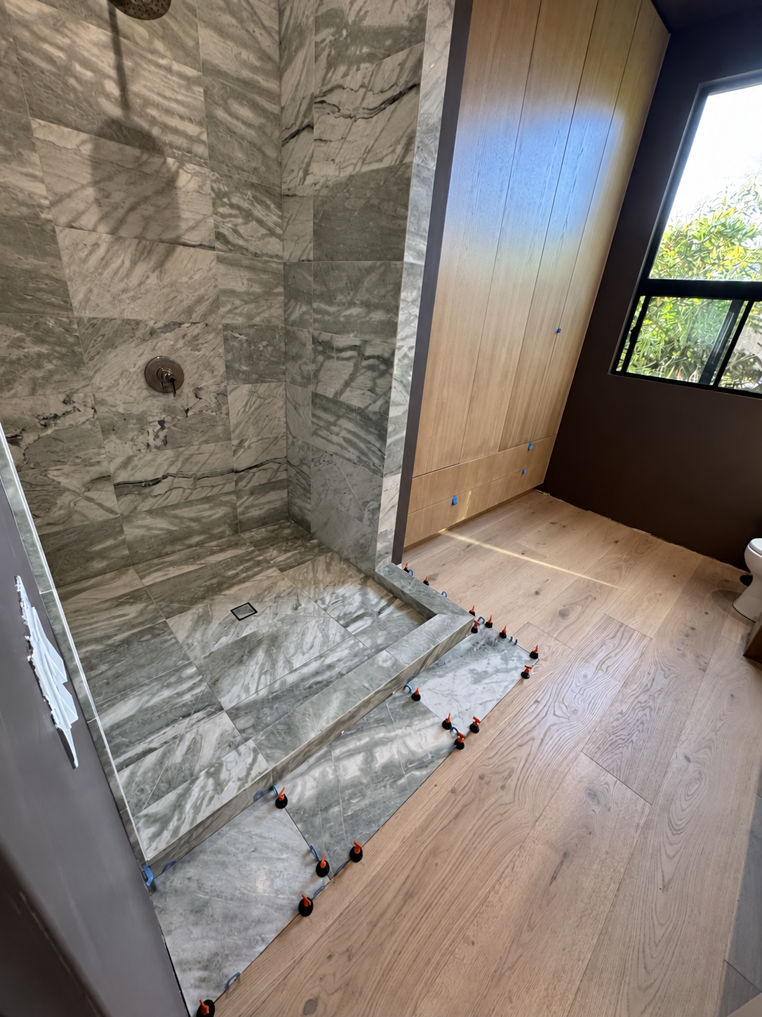 Custom shower with veined green-gray stone tile walls, a matching tiled curb, and an envelope-cut shower floor